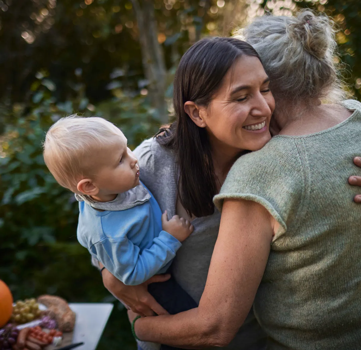 A woman hugs another while holding a baby