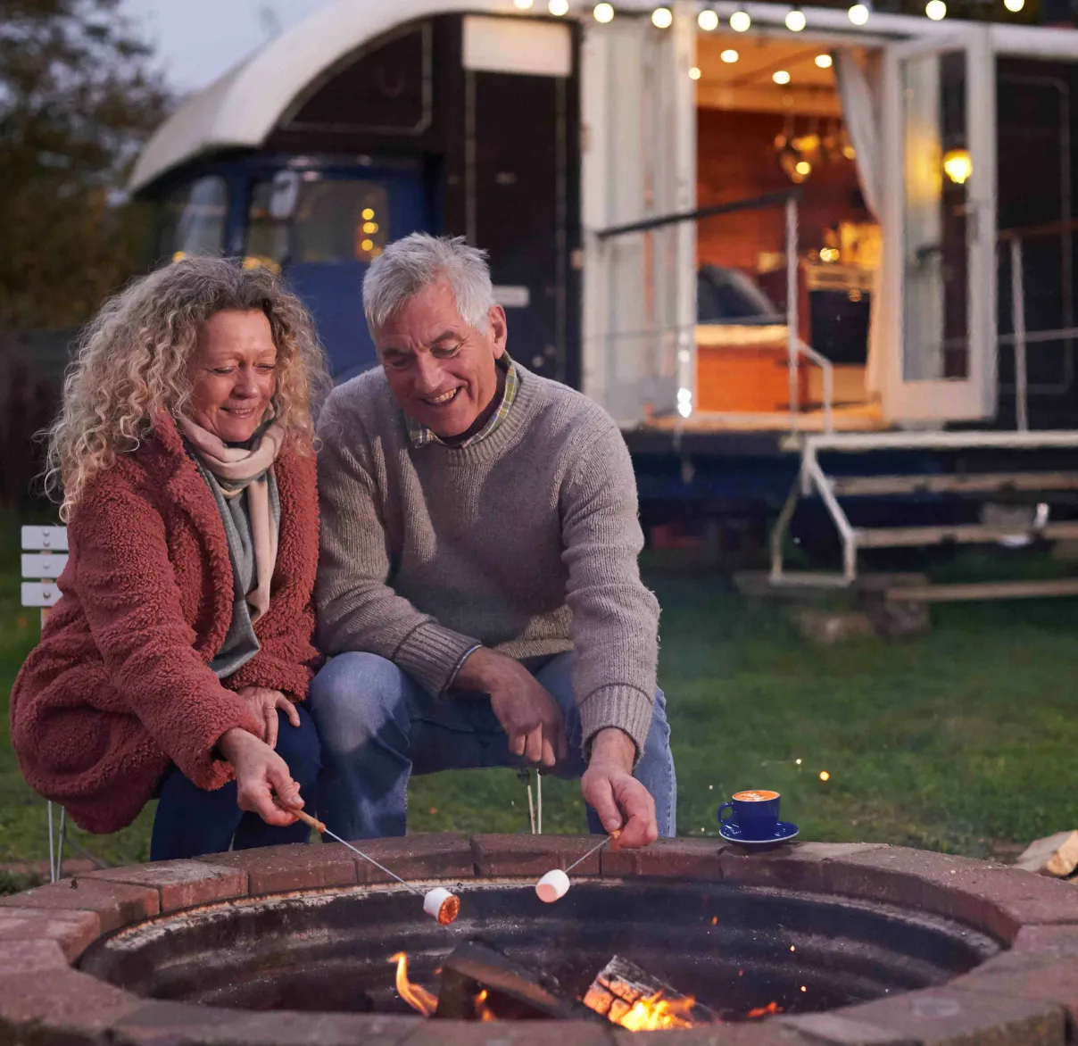 A couple sitting happily around a camp fire with coffee and holiday home