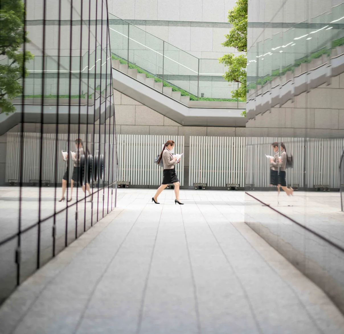 An office worker walks between buildings in the city, their figure reflected on the glass of the buildings around them