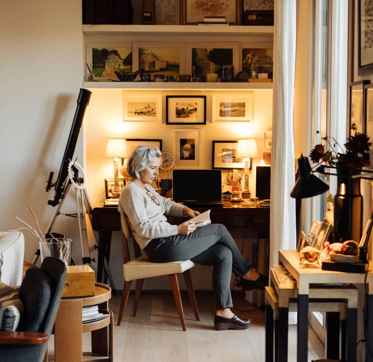 A lady reads a book in a study nook of her well furnished home