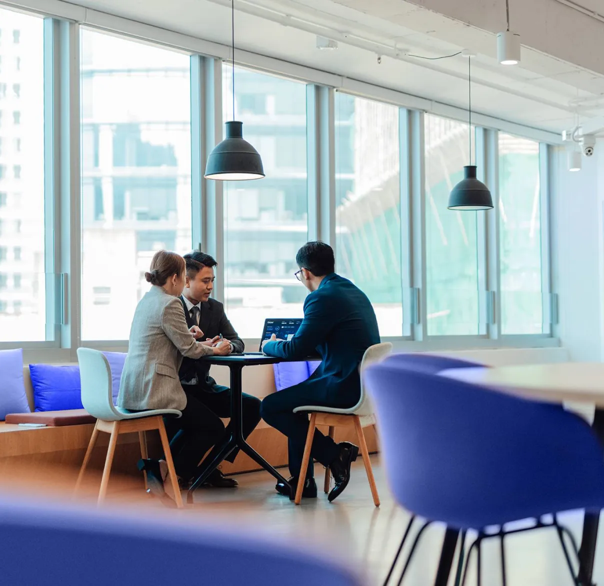 Three colleagues meeting in an office sitting down at a table together talking