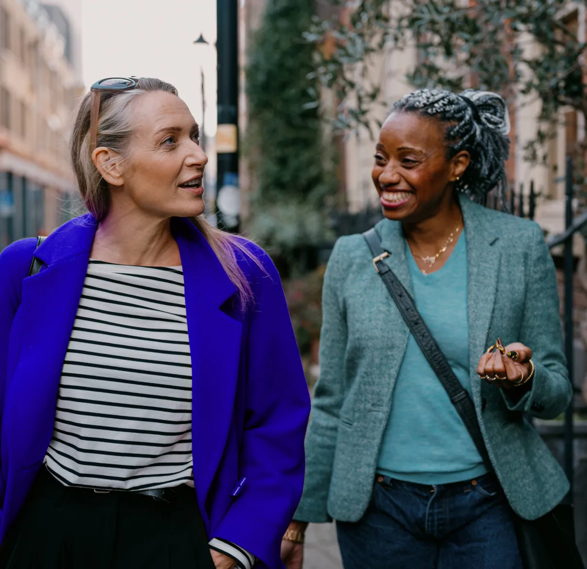 Two women walk along a suburban American street talking and laughing