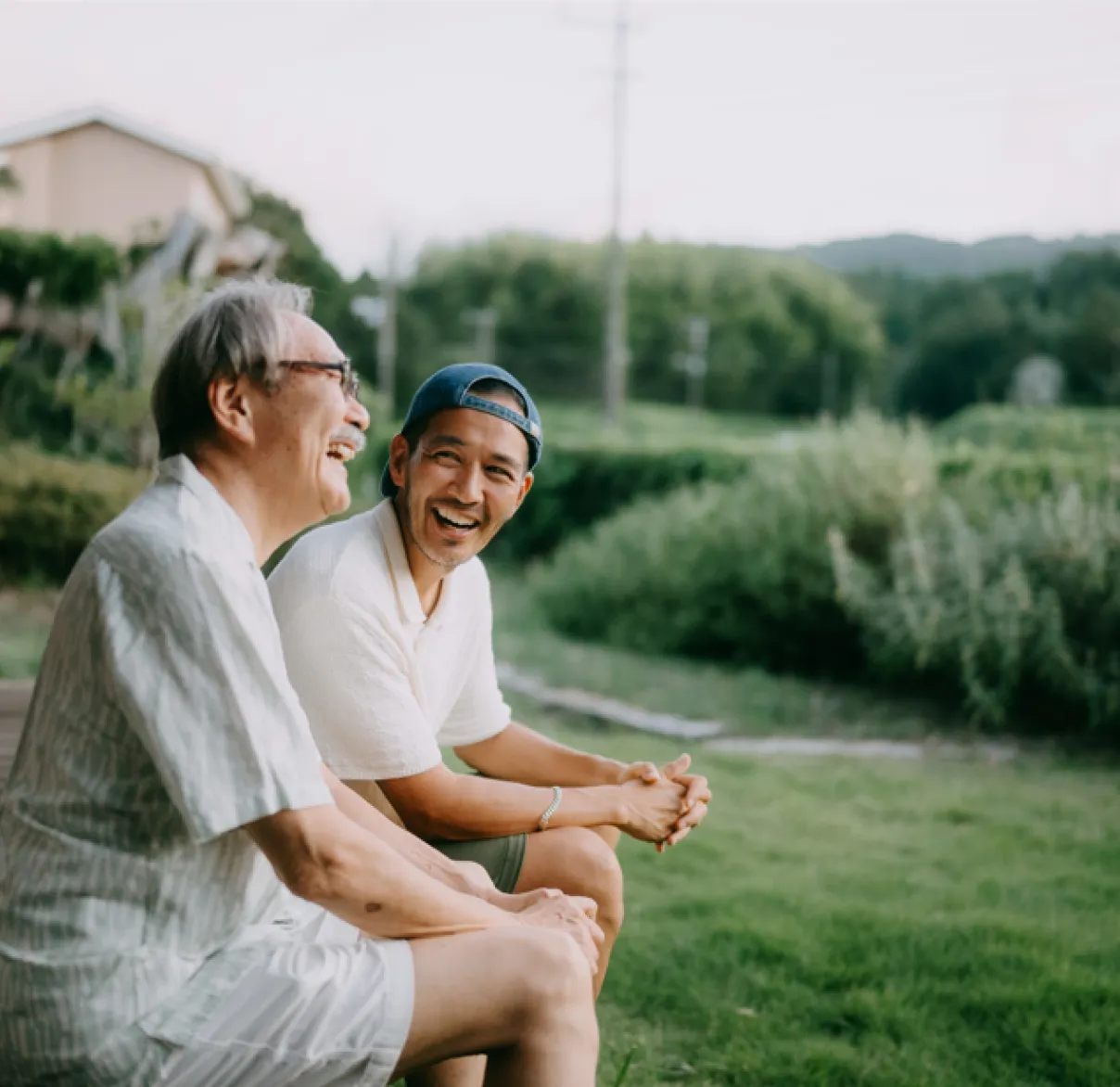 A father and adult son laughing together in a countryside setting