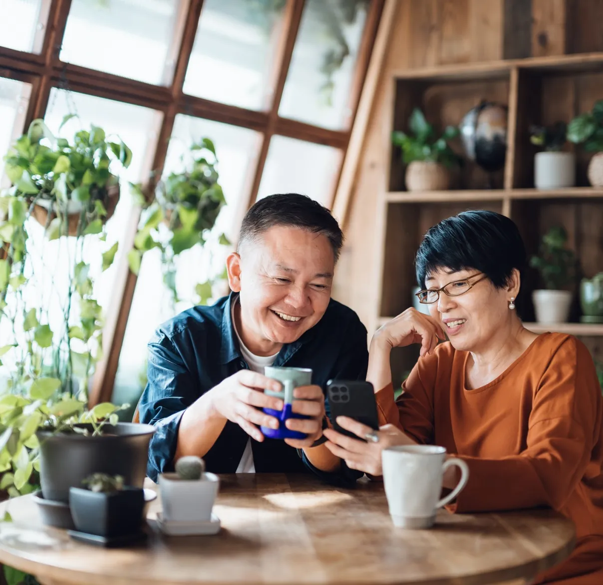 Two people reviewing financial information on a smartphone at a table at home as part of preparing for retirement and planning future income