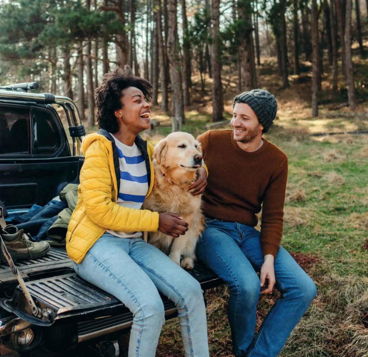 A couple sit on the back of their pick-up truck with their dog in the outdoors