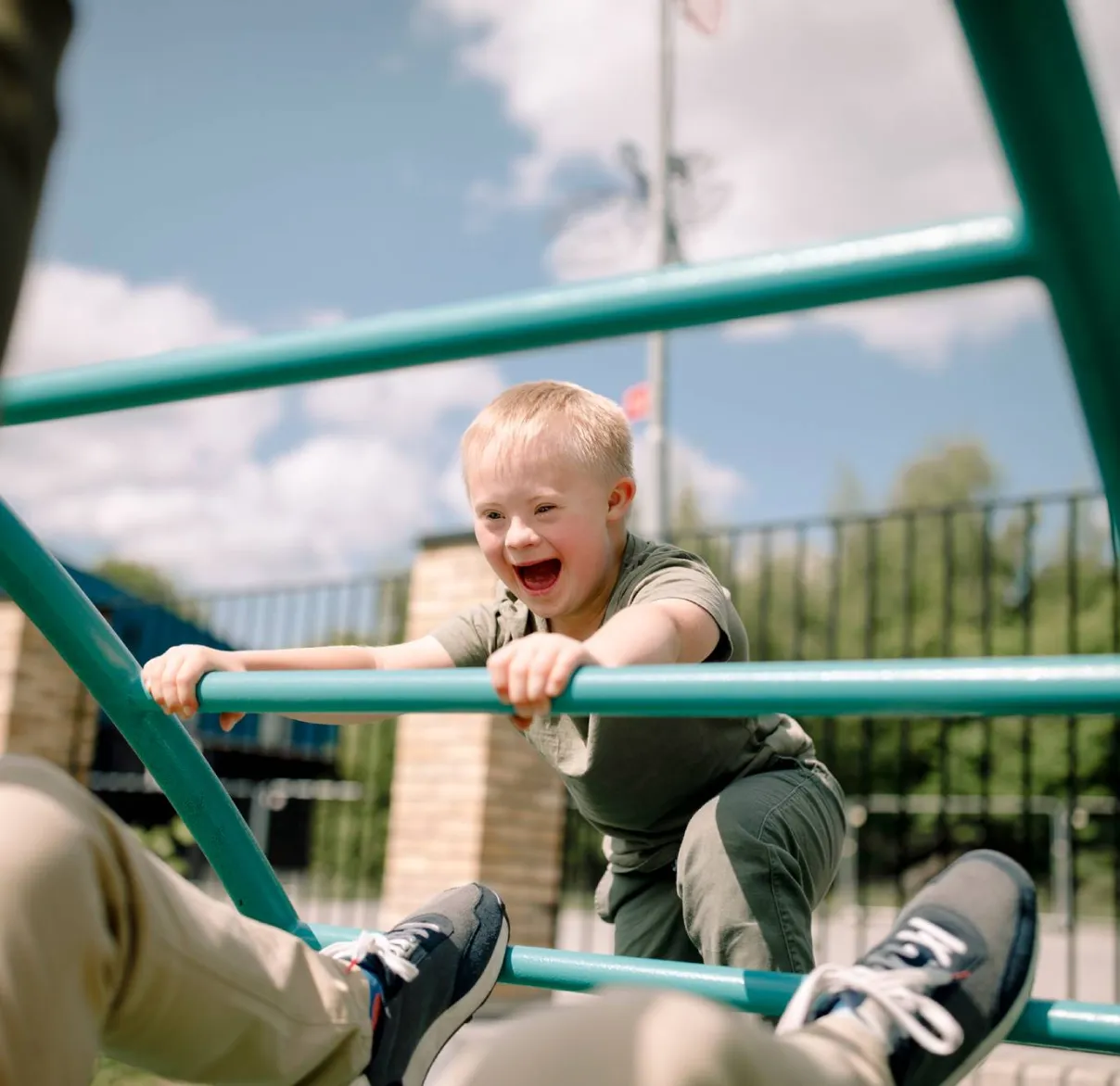 A boy with down syndrome plays on a playground climbing frame with his parent