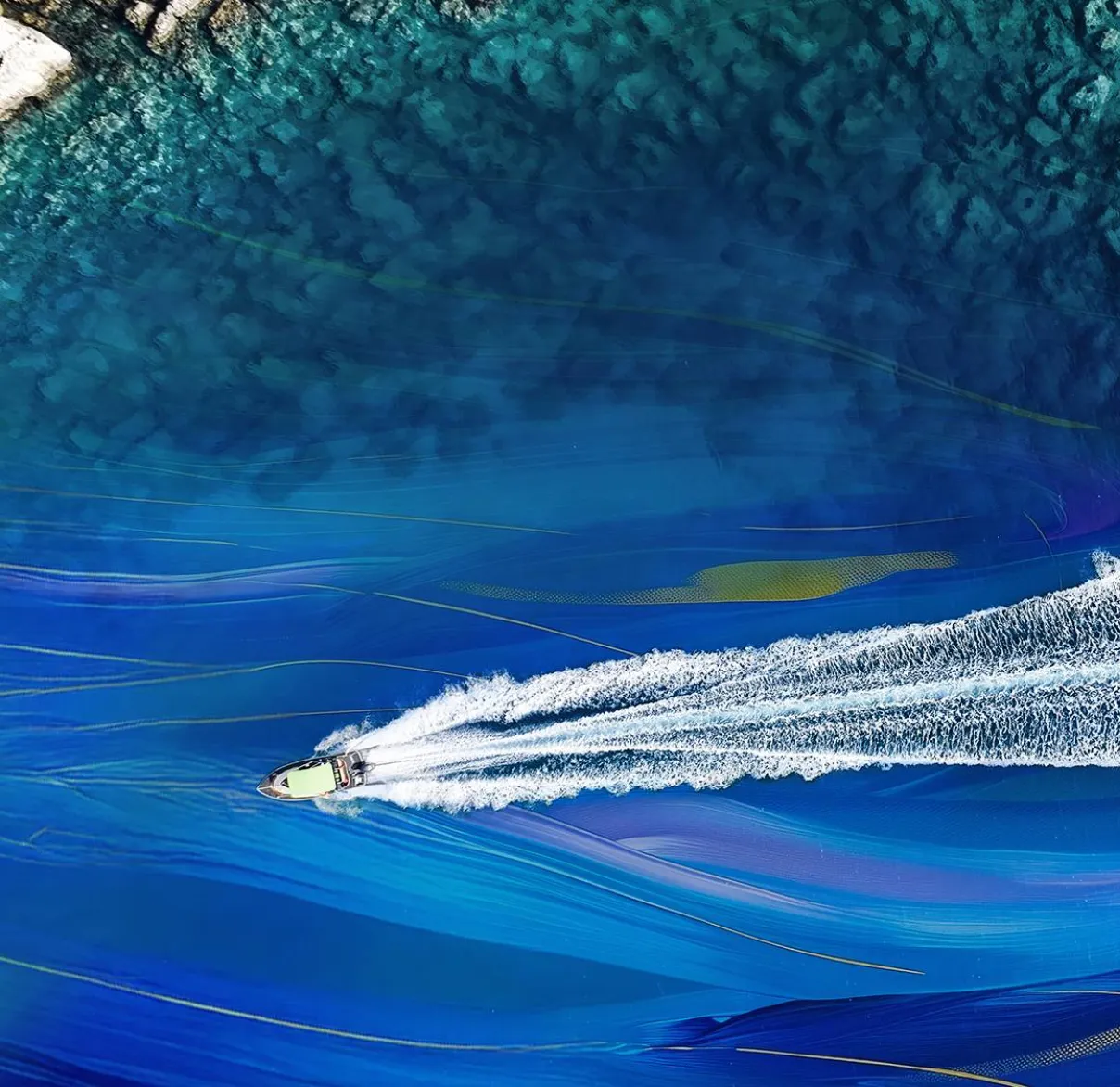 A bird's eye view of a boat cutting through waters near to a rocky coastline