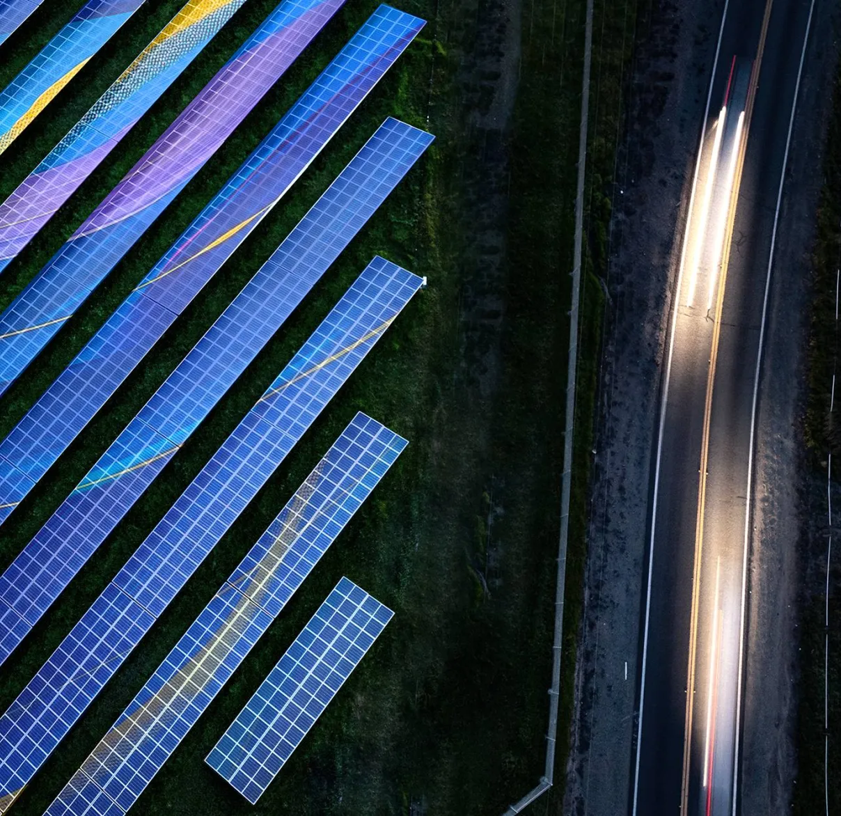 A bird's eye view of a solar farm next to a busy road at dusk