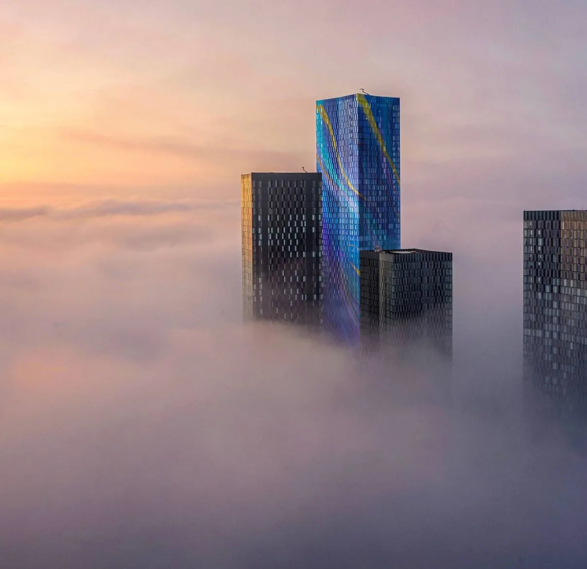 The tops of skyscrapers poke through fog at sunrise over a city