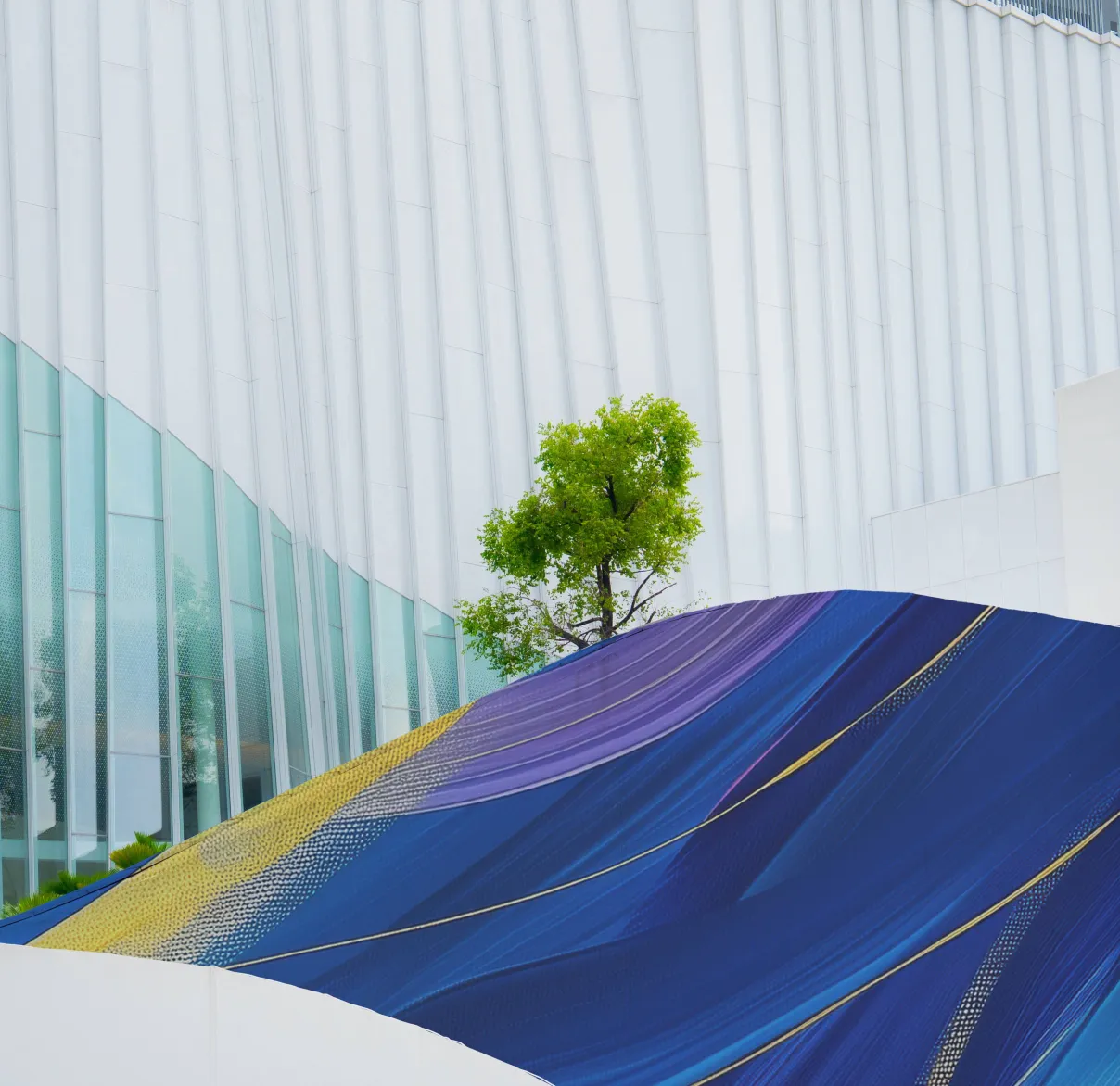 A lime green tree peaks out from behind a colourful wall of a modern corporate office