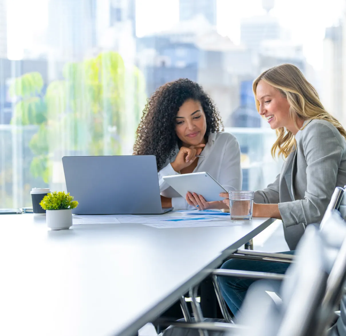Female advisers checking documents on tablet and laptop in meeting room