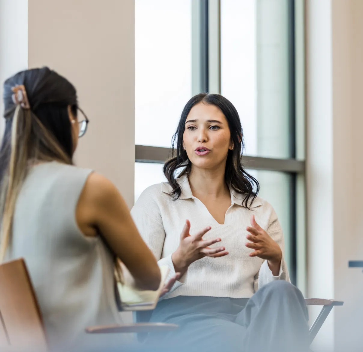 Two women talk with one another while sat down in an office building