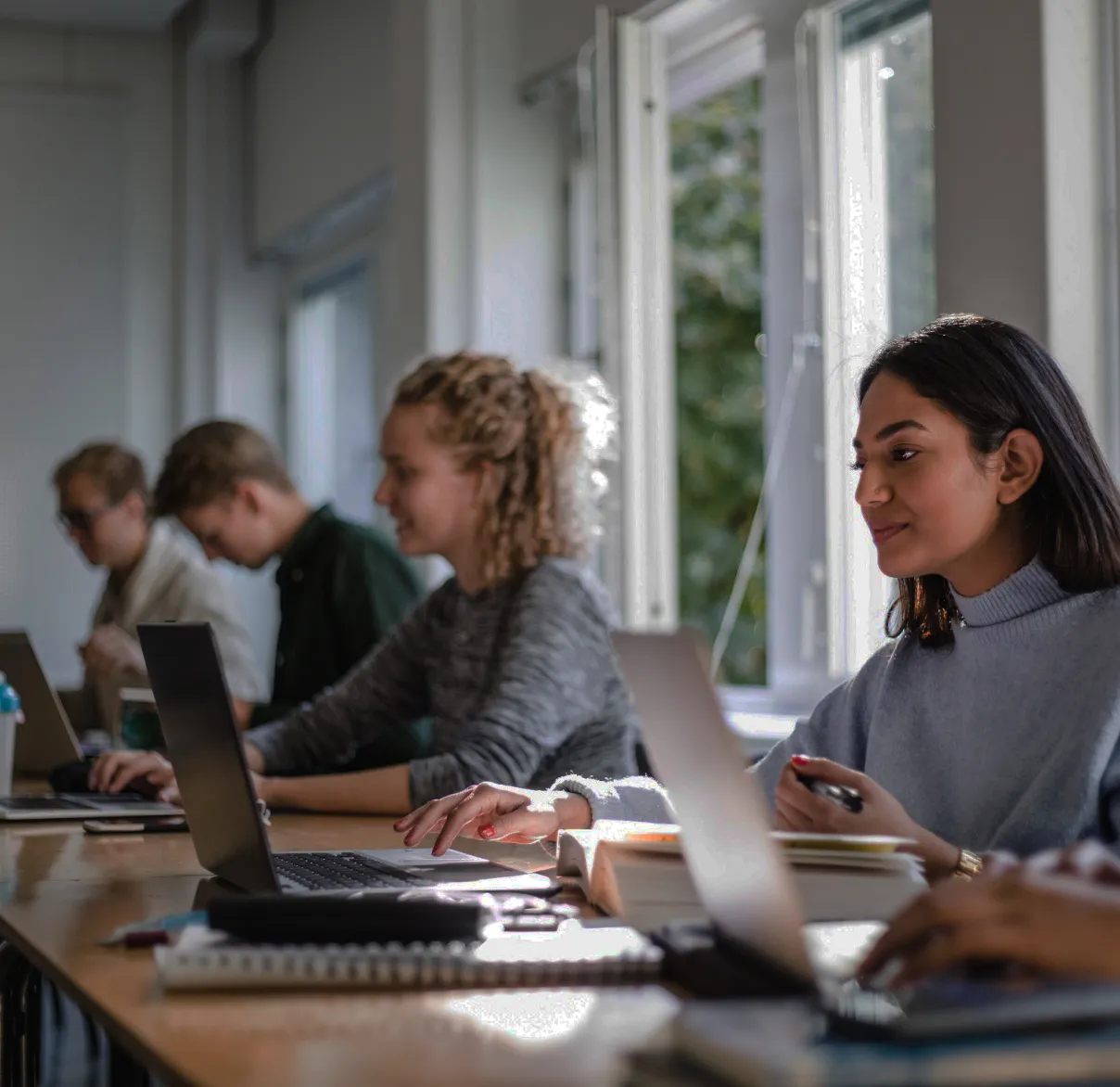 Students sit in a classroom while working on their books and laptops