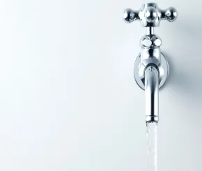 Minimalist image of a shiny chrome wall-mounted faucet with water flowing, set against a smooth white background
