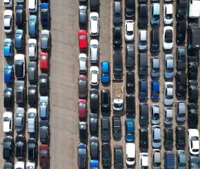 Aerial view of a densely packed parking lot filled with rows of parked cars in various colors and sizes, arranged in parallel lines on a concrete surface.