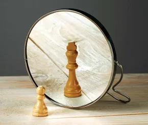 A small wooden chess pawn looking into a mirror and seeing the reflection of a king piece, symbolizing self-confidence, ambition, and inner potential.