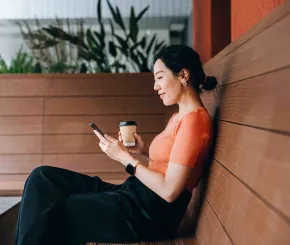 A young and professional woman .looks at her phone while having a coffee on bench seating