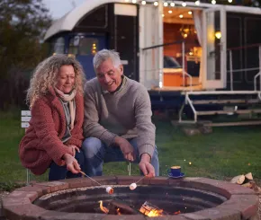 A couple toast marshmallows on an open fire in front of their campervan