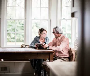 A father and daughter have a discussion at a pub table while looking at something on an iPad