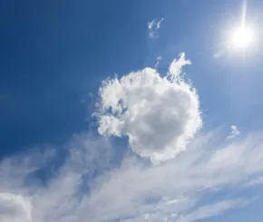 A bright blue sky with the sun shining in the top right corner and a single fluffy white cloud centered prominently, surrounded by wisps of thinner clouds.