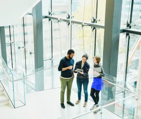 Thee office workers talk on the stairs of a glass corporate office building