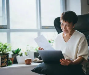 A lady reading a laptop and documents while seated in her home