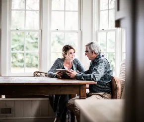 An investment manager giving advice to a man at the table in his kitchen by some large windows
