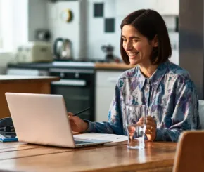 A young woman smiling at her laptop whilst sat at her kitchen table