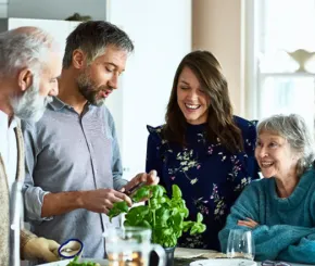 A family made up of two elderly parents and their two adult children cooking together happily