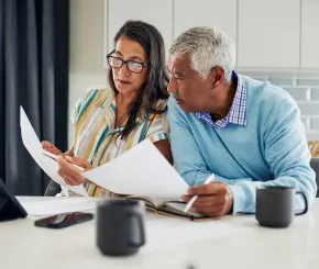 A couple review paperwork at their kitchen bench with coffee and a tablet
