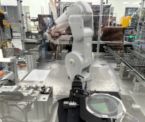 Industrial robotic arm operating inside a glass‑enclosed manufacturing cell, handling components on a precision assembly workstation.