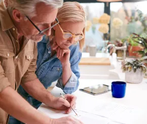 Older couple signing paperwork in their kitchen