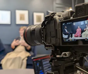 Photo of camera with two women in discussion about a topic