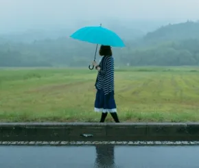 A lady holds an umbrella while walking along water soaked fields