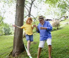 Grandfather holding the hand of his granddaughter as she is slacklining