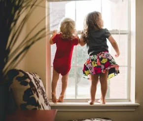 Two children stand up to look out the window in a home