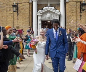 A newly married couple walk through a line of people throwing petals at them