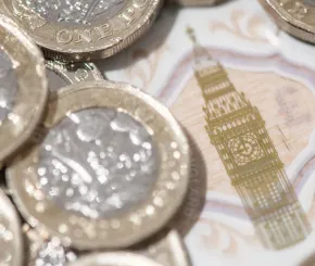 pound coins piles on top of each other with a note behind with Big Ben central