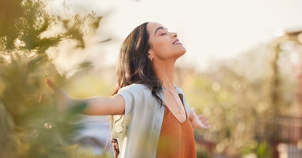 image of a woman at peace in an idyllic scene outdoors in nature standing with arms spread wide with a sense of freedom
