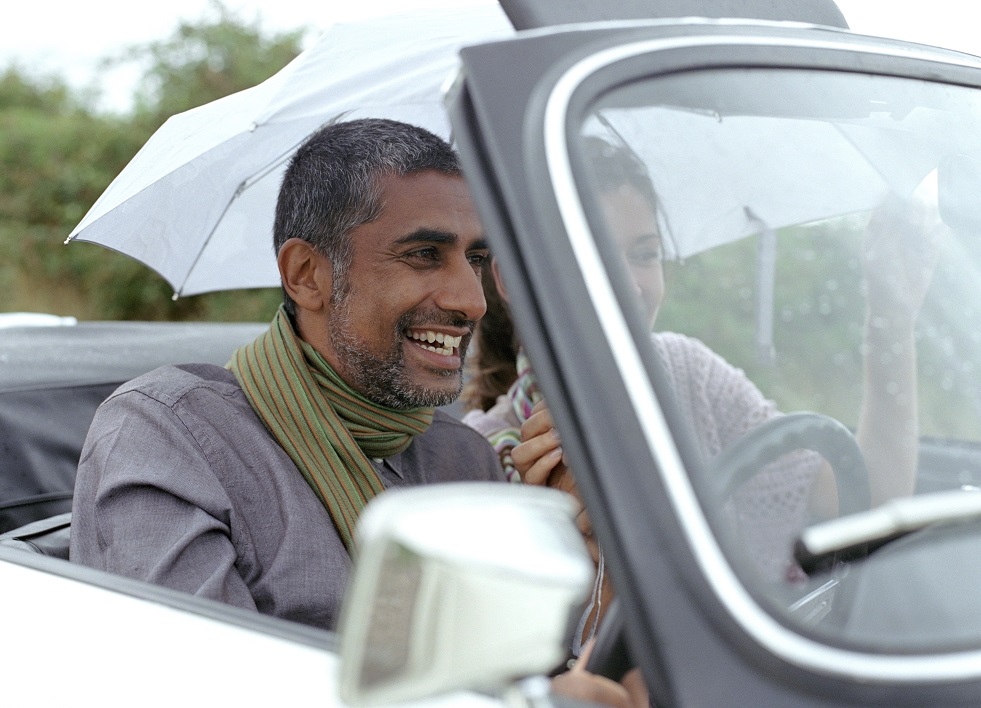 A man and women laugh as they sit in their convertible car under an umbrella as it rains