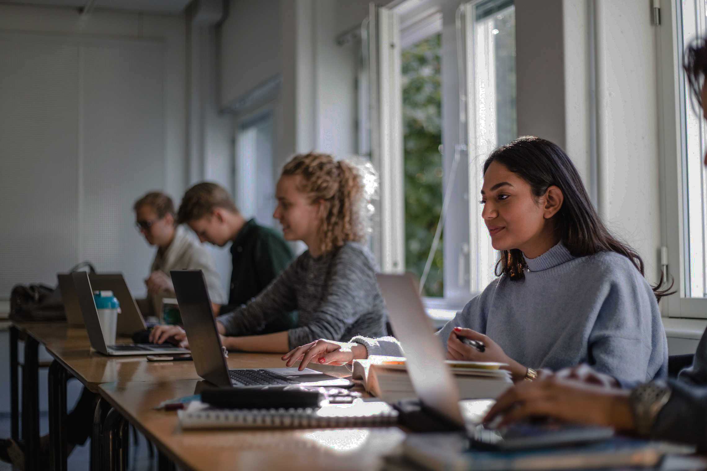 Students sit in a classroom while working on their books and laptops