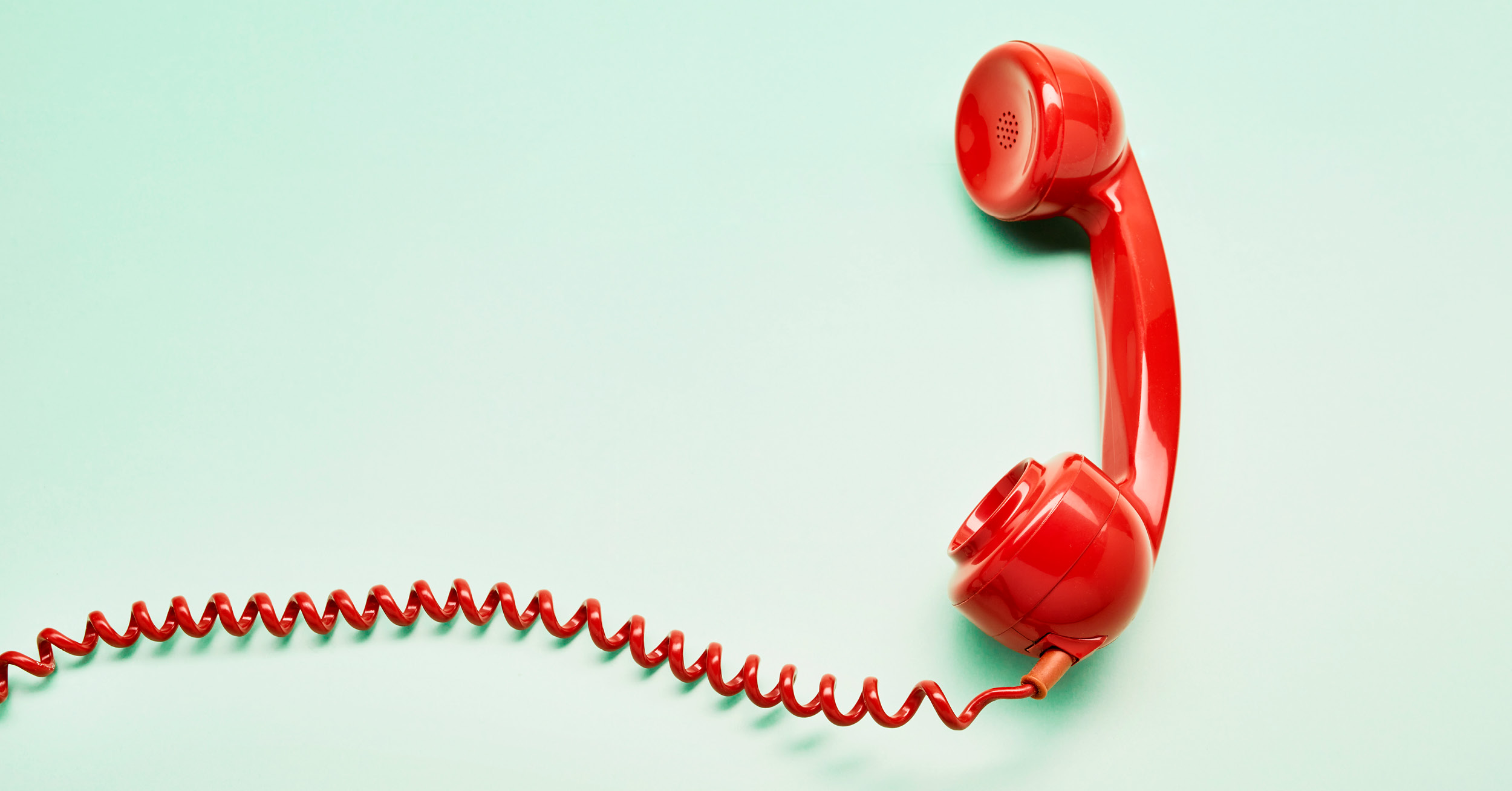 Red mid-century telephone receiver on mint green background with coiled wire flowing off canvas to the left.
