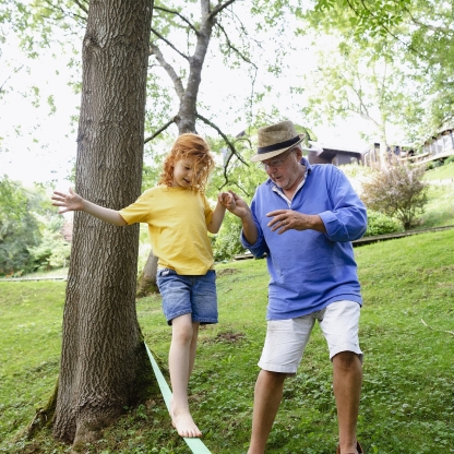 Grandfather holding the hand of his granddaughter as she is slacklining